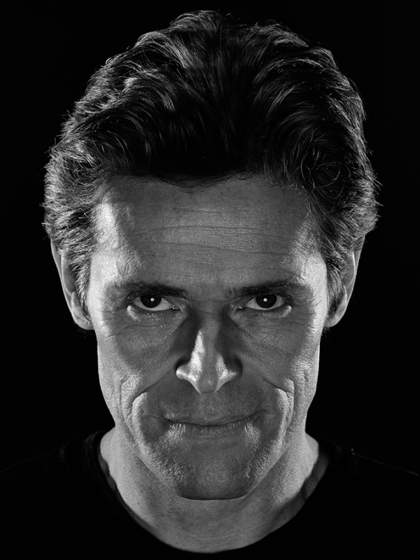 Close-up monochrome portrait of actor Willem Dafoe with dark background and dramatic high-contrast lighting by Andrew Macpherson.