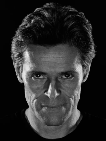 Close-up monochrome portrait of actor Willem Dafoe with dark background and dramatic high-contrast lighting by Andrew Macpherson.