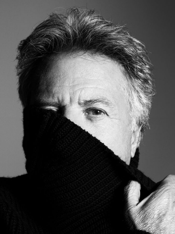 Portrait of an adult male with grey hair partially obscuring his face with a dark knit turtleneck sweater in a black and white photograph.