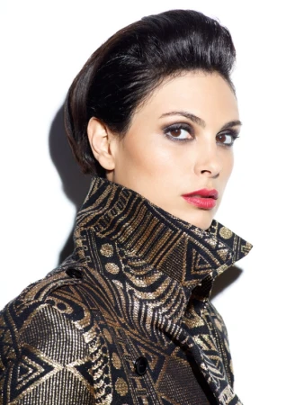Close-up portrait of Morena Baccarin wearing a high-collared patterned metallic trench coat against a white background