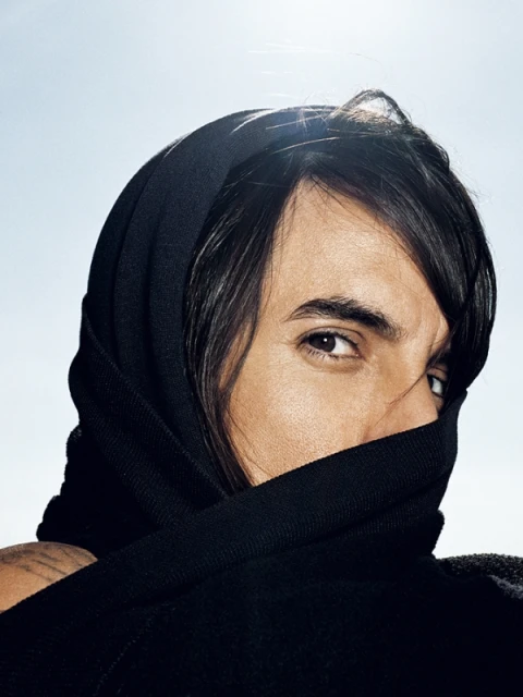 Close-up portrait of an adult with dark hair and a dark head covering, part of the face is covered with the head covering, sky background.