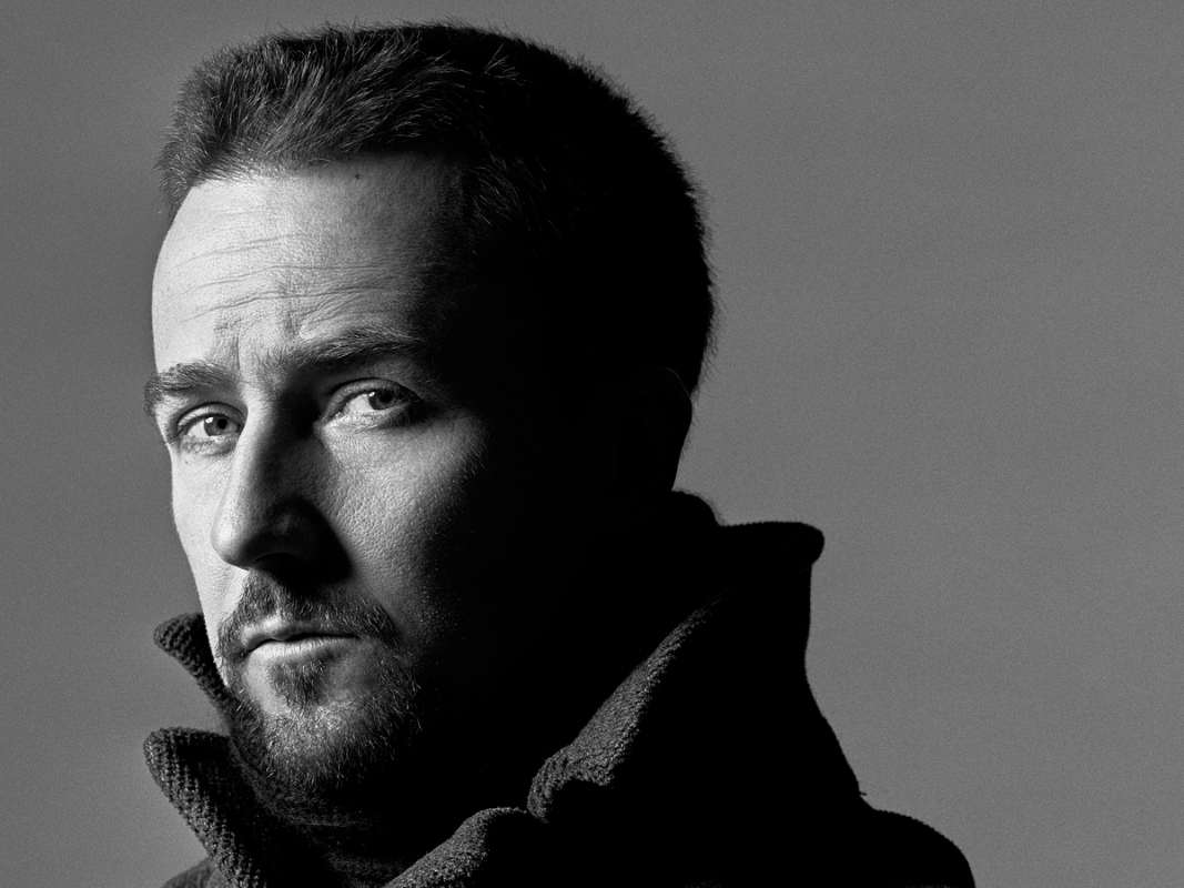 Black and white portrait of an adult man with dark hair and a beard, wearing a high-collared coat, set against a neutral grey backdrop.