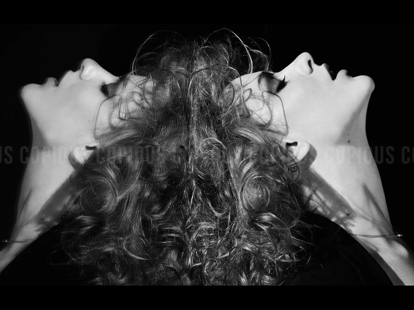 Black and white portrait of a woman with curly hair photographed in profile against a dark background, by Andrew Macpherson.
