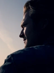 Close-up profile of a man in silhouette against a clear sky, captured in a dramatic cinematic portrait.