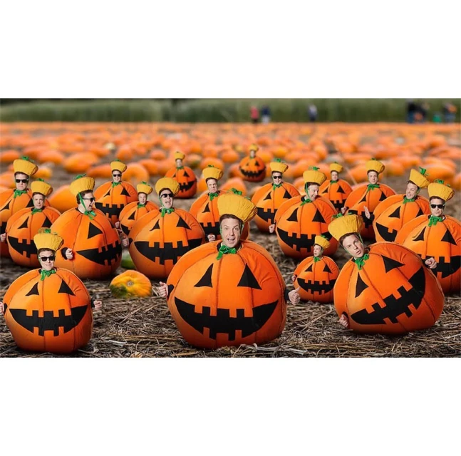 Group of people dressed in smiling pumpkin costumes, gathered in a pumpkin patch for a festive Halloween-themed event.