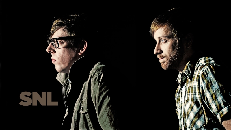 Profile portrait of two men against a black background with dramatic low-key lighting and visible SNL logo