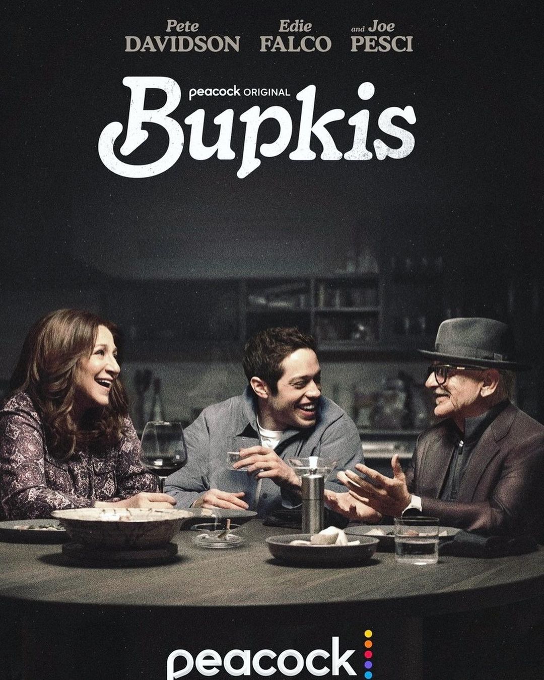 Poster art from the Peacock original television series, Bupkis, featuring Pete Davidson, Edie Falco, and Joe Pesci sitting at a table.