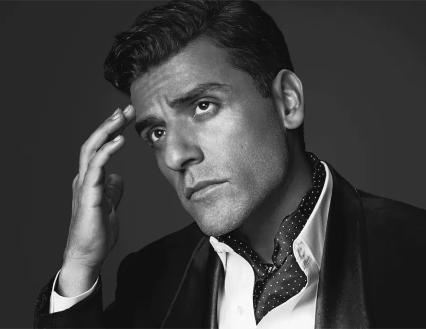 Monochrome close-up portrait of a thoughtful adult male with fair skin, wearing a suit jacket and patterned cravat, against a gray backdrop.