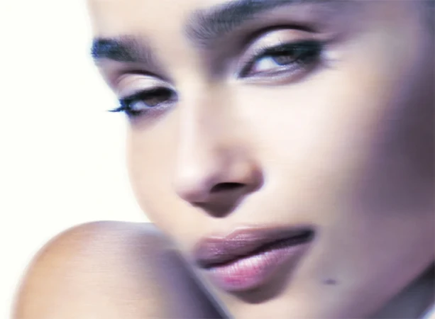 Close-up portrait of Zoë Kravitz with dark eye makeup and soft lighting against a minimal background