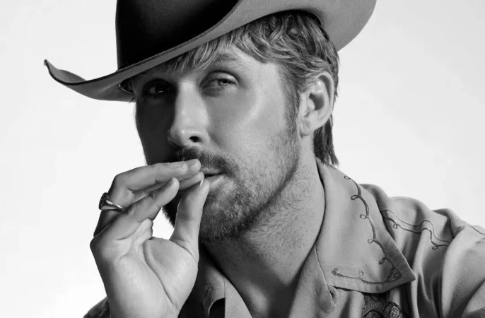 Close-up monochrome portrait of a man wearing a cowboy hat and embroidered shirt, holding his hand near his mouth.