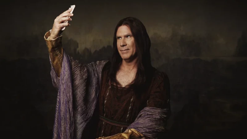 Man dressed as Mona Lisa taking a selfie with a smartphone. He has long brown hair, wearing a brown dress with a landscape background.