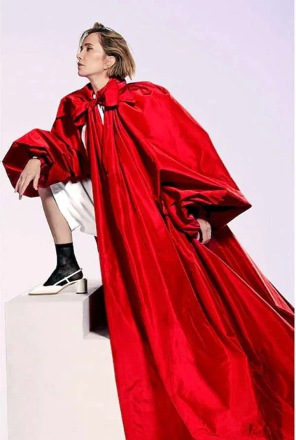 Woman in dramatic red cape posing on white platform. Close-up shot with bold fashion and simple studio backdrop, evoking editorial style.