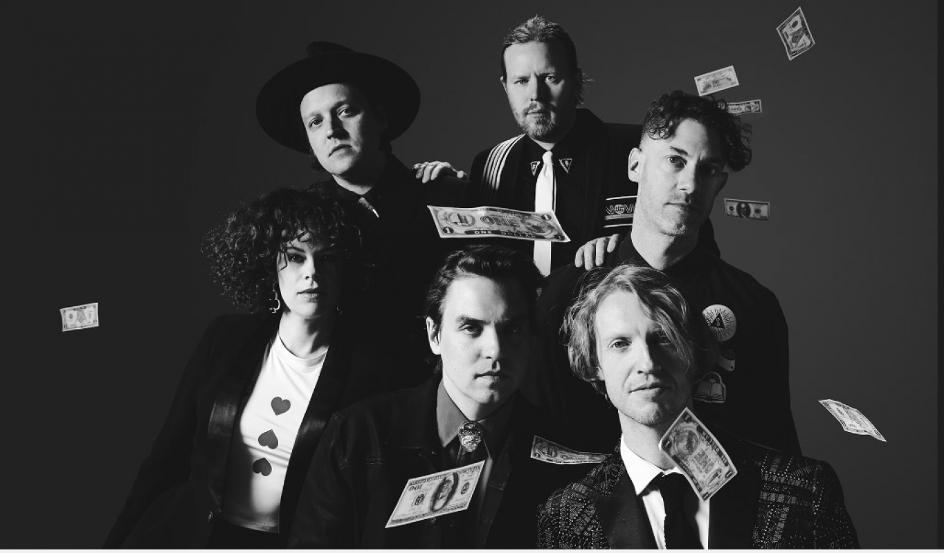 Black and white portrait of a group of five people indoors with money floating around them in a dimly lit indoor setting.