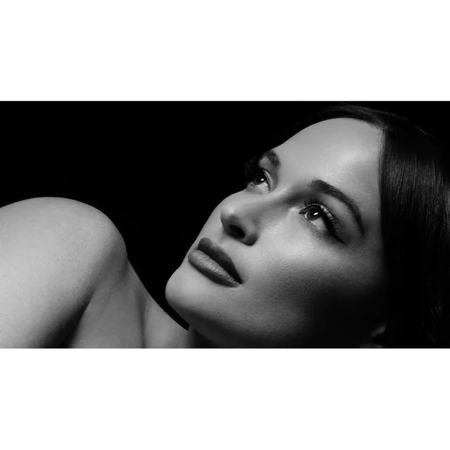 Monochrome portrait of a woman gazing upwards with soft lighting that highlights her features against a dark background.