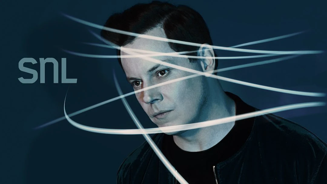 Portrait of an adult male with dark hair wearing a black bomber jacket with light lines digitally added over a dark blue background.