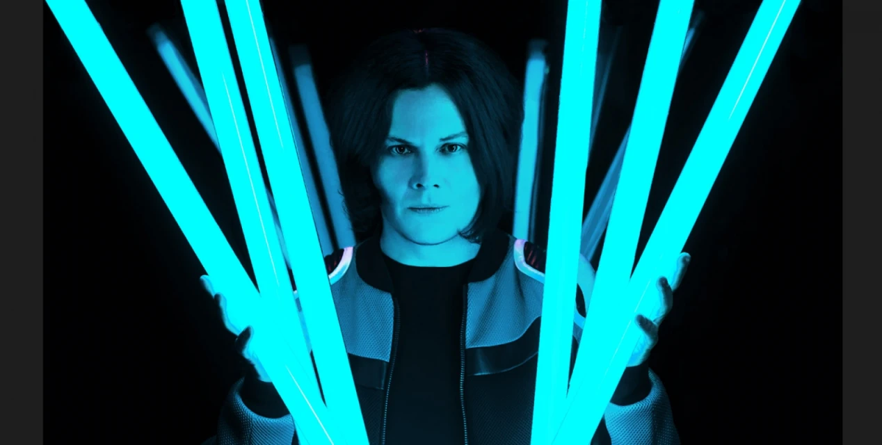 Portrait of adult male in blue-toned studio lighting, with multiple cyan-colored fluorescent tubes in the foreground, set against a dark backdrop.
