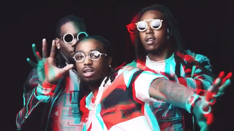 Three African American men with sunglasses are indoors against a dark backdrop. They are wearing casual fashion with jewelry and light makeup.