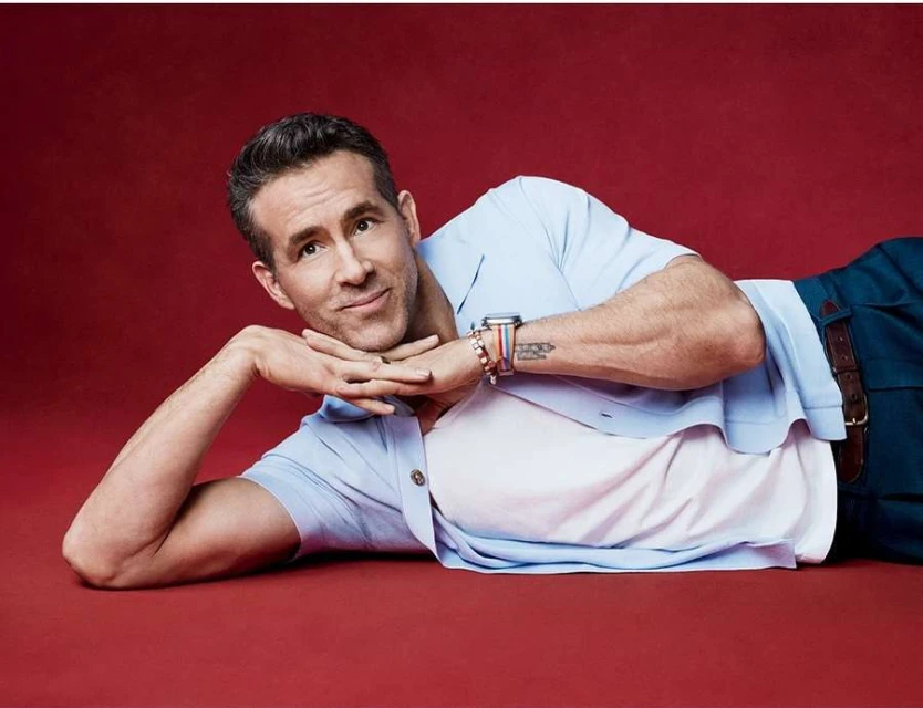 Adult male with short hair laying down in a light blue shirt and dark pants on a red surface, looking at the camera with a slight smile.