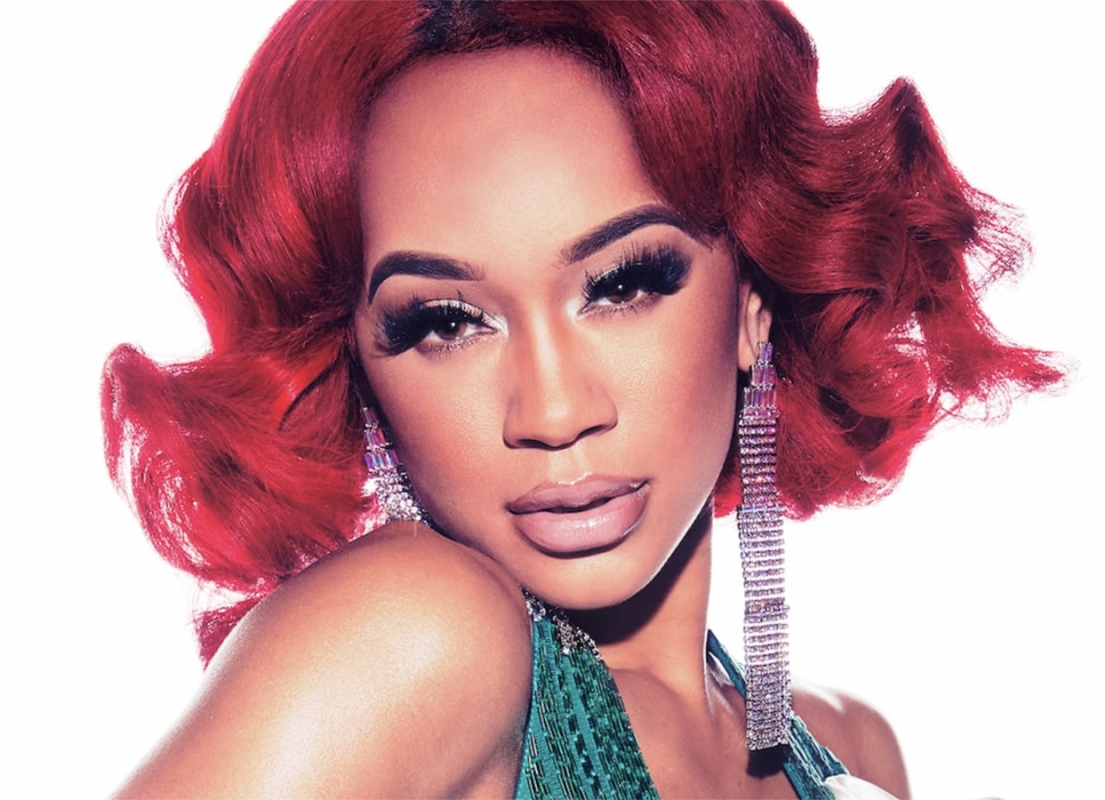 Close-up of an adult female with bright red hair, dramatic lashes, and crystal earrings against a clean white backdrop.