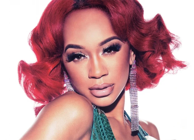 Close-up of an adult female with bright red hair, dramatic lashes, and crystal earrings against a clean white backdrop.