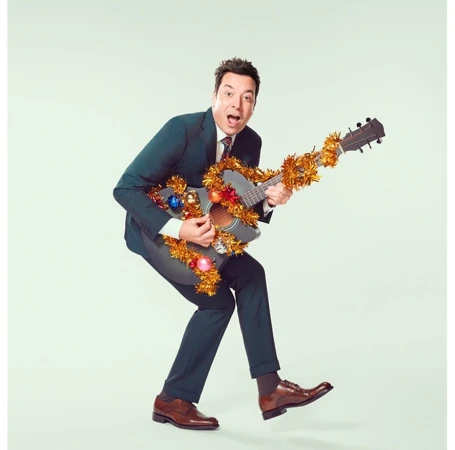 Enthusiastic man in suit plays guitar with Christmas garland and ornaments, posing in front of a light background in a studio.