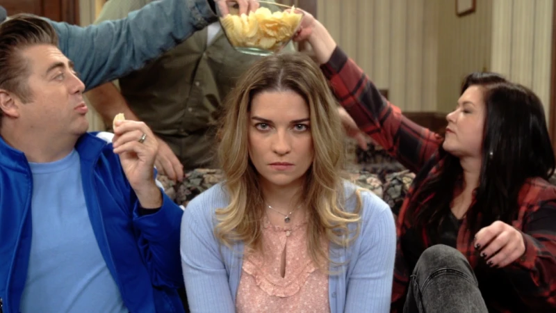 Woman surrounded by people and chips inside of a living room. The woman has an angry expression with two other people next to her.