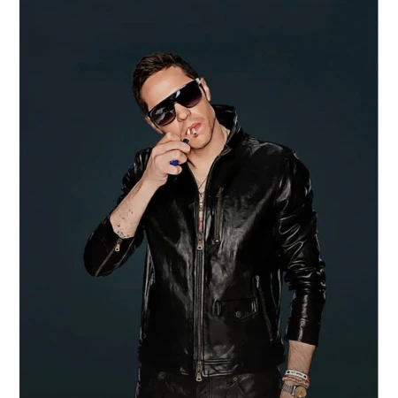 Man wearing sunglasses and a black leather jacket lighting a cigarette against a dark background