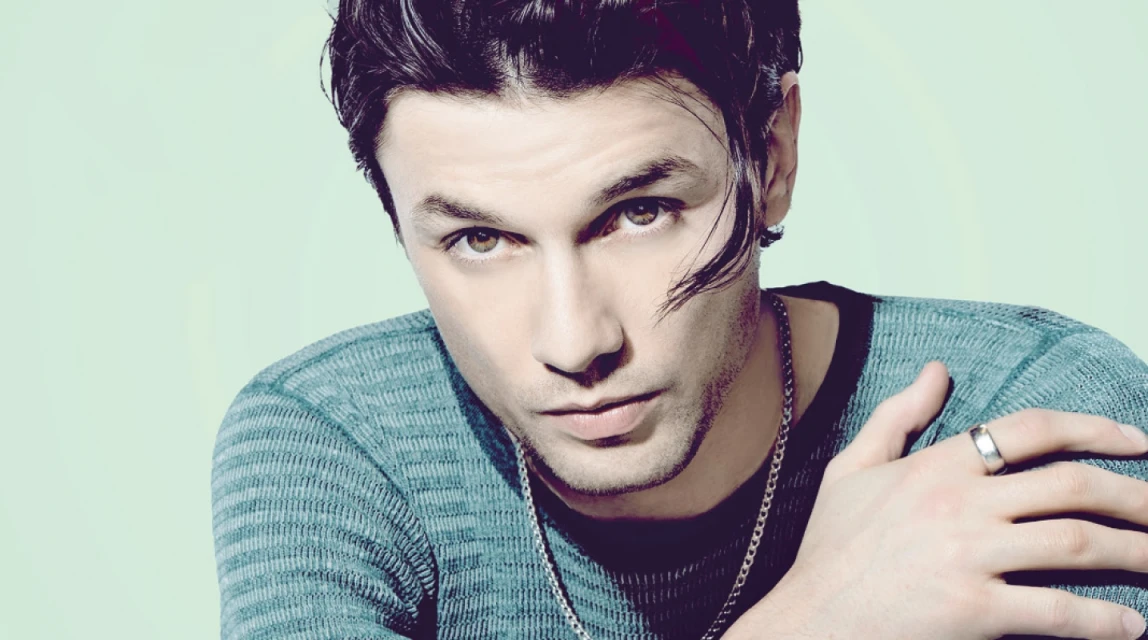 Close-up studio portrait of a dark-haired, fair-skinned adult male with green eyes wearing a green shirt, silver chain, and ring.