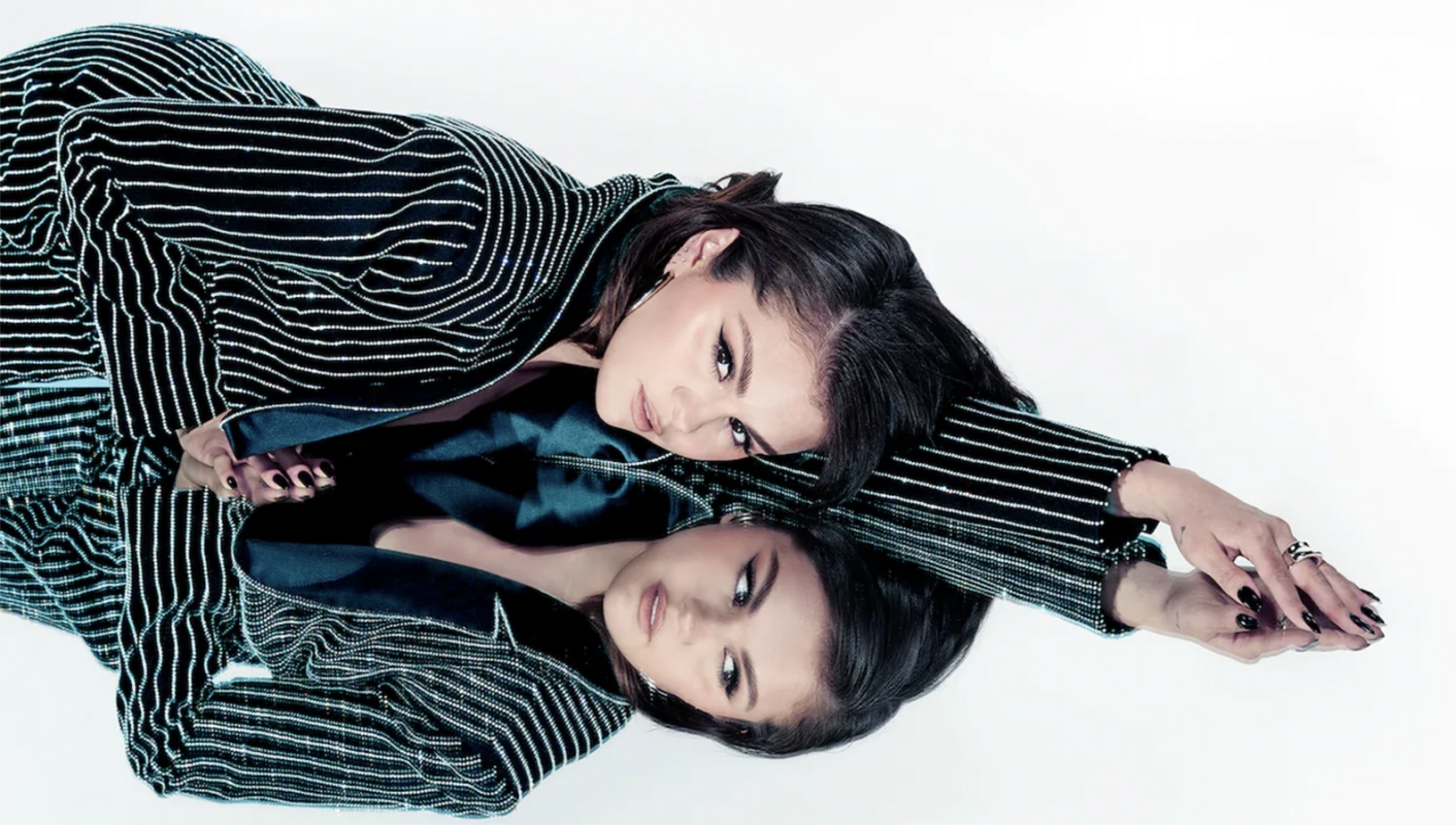 Glamorous photo of a young woman with dark hair in a black and white striped jacket, laying on a reflective surface in a white photo studio.