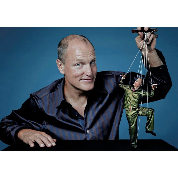 Actor Woody Harrelson with marionette of himself in green striped pajamas against blue background, manipulated by unseen puppeteer.