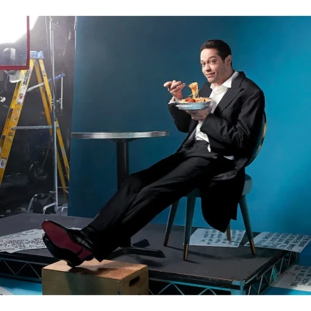 Pete Davidson eating spaghetti from a foil takeout container on a studio set, photographed by Mary Ellen Matthews.