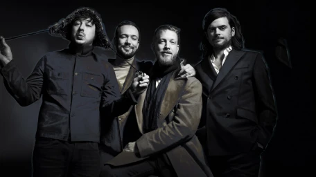 Portrait of four men posing together against a dark background, photographed by Mary Ellen Matthews.