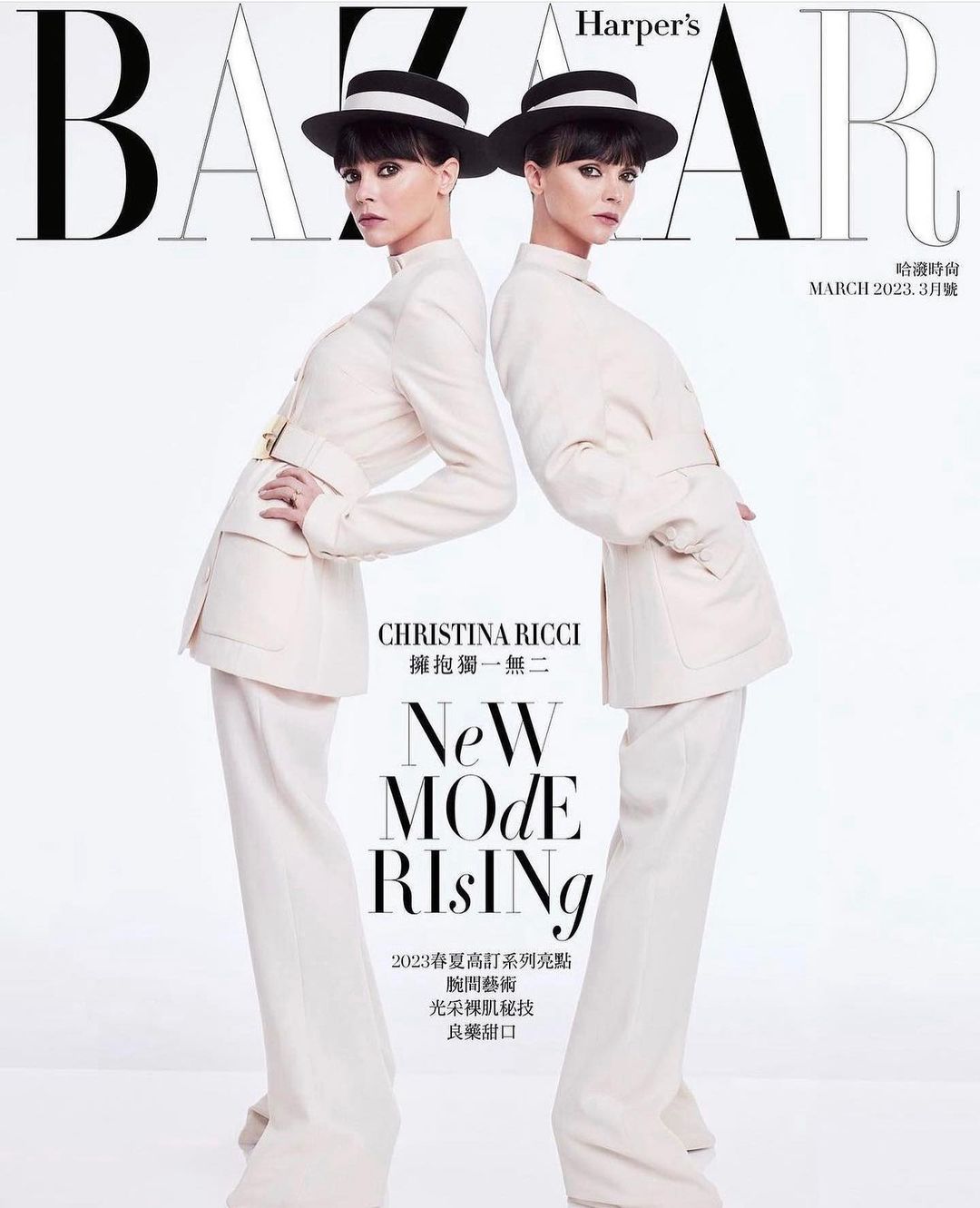 Two women posing on a fashion magazine cover wearing cream-colored suits, black hats, and dark hair against a white background.