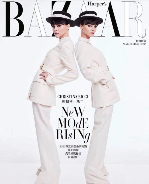 Two women posing on a fashion magazine cover wearing cream-colored suits, black hats, and dark hair against a white background.