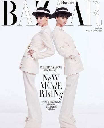 Two women posing on a fashion magazine cover wearing cream-colored suits, black hats, and dark hair against a white background.