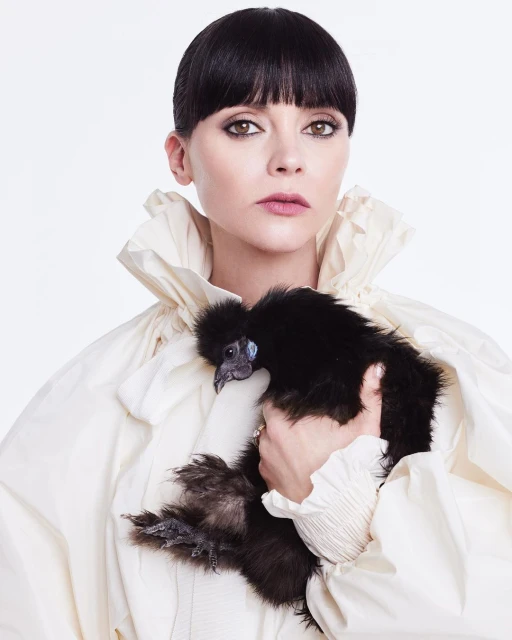 Woman in white ruffled dress holds black silky bantam chicken in light studio portrait. The chicken is held at chest height.