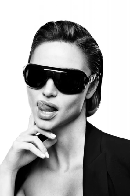 A woman with wet hair and dark sunglasses poses with her tongue sticking out in a studio portrait with bright white background.
