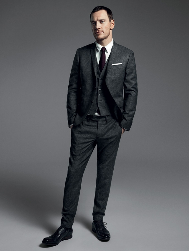 Adult male in a three-piece suit with a tie, standing in a photo studio with hands in pockets, wearing dress shoes. Full-length studio portrait.