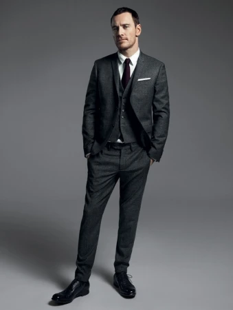 Adult male in a three-piece suit with a tie, standing in a photo studio with hands in pockets, wearing dress shoes. Full-length studio portrait.