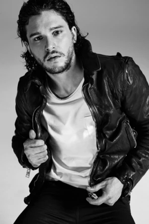 Portrait of Kit Harington wearing a black leather jacket and white t-shirt against a light seamless background.