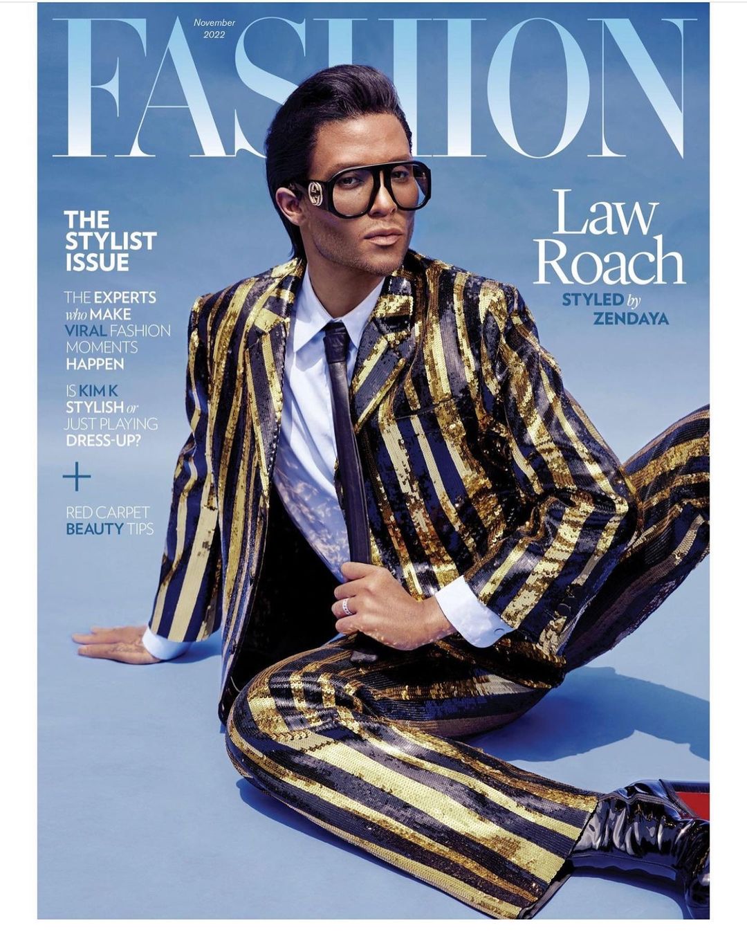 Magazine cover featuring Law Roach in a gold-striped suit, tie, and Gucci sunglasses, seated against a blue backdrop. Fashion editorial.