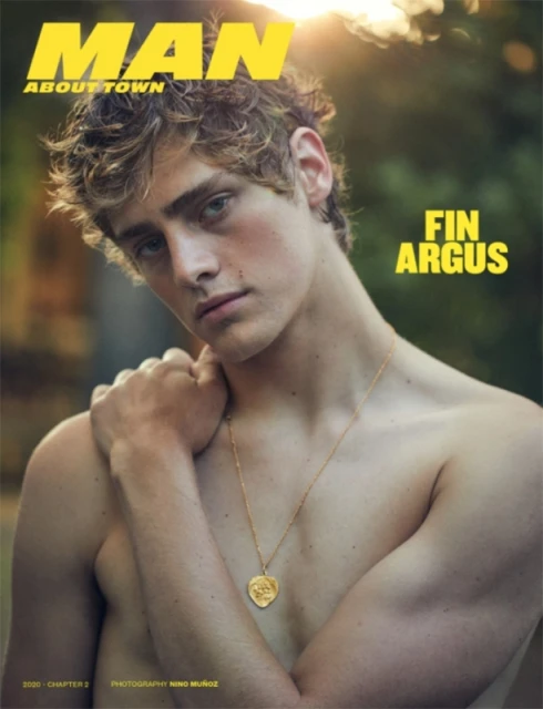 Magazine cover featuring a shirtless male model with a gold necklace against a blurred outdoor background and bright sunlight.