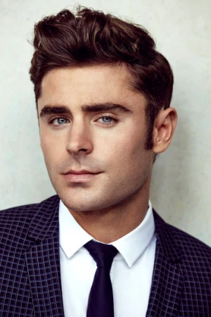 Portrait of Zac Efron wearing a dark patterned blazer, white dress shirt, and dark tie against a light neutral background.