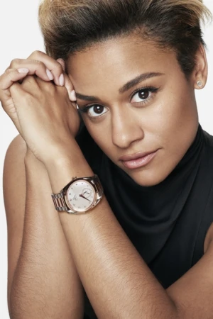 Close-up portrait of a woman wearing a metallic watch, posing with hands near her face against a white background