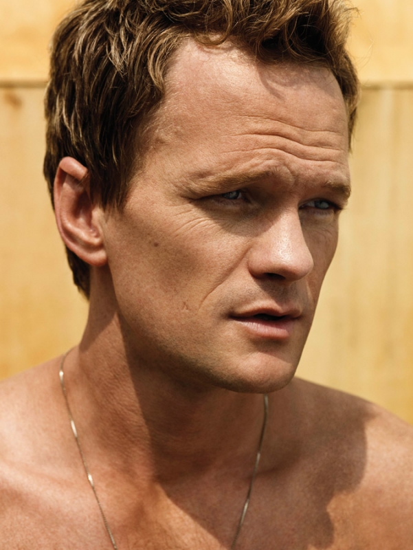 Close-up portrait of a fair-skinned adult male with short brown hair, wearing a thin necklace, against a neutral background.