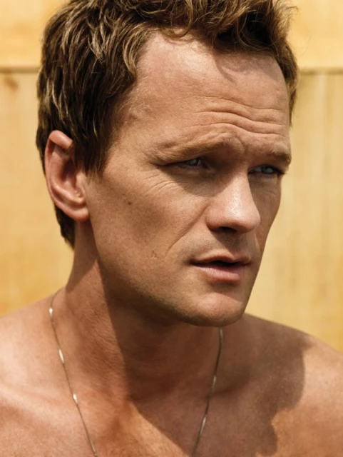 Close-up portrait of a fair-skinned adult male with short brown hair, wearing a thin necklace, against a neutral background.