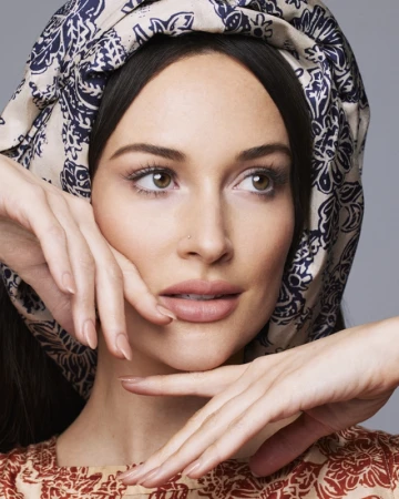 Close-up portrait of a woman wearing a blue and white patterned headscarf and resting her hands gently beneath her chin.