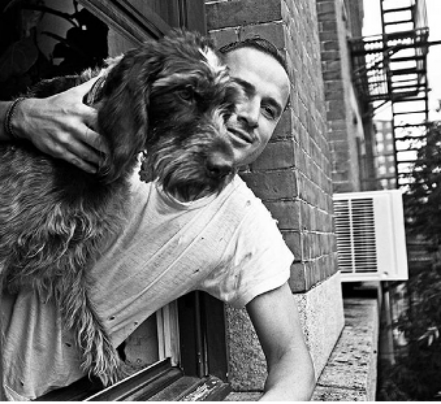Monochrome photo of a man embracing a dog by a window in a brick building, creating a personal and intimate moment.