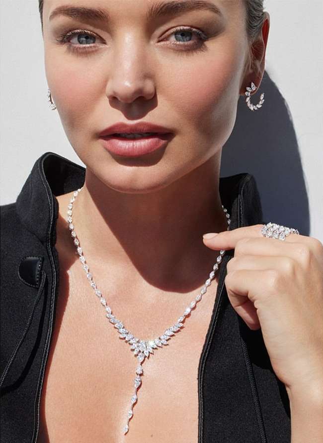 Close-up portrait of a woman wearing diamond drop earrings, a diamond necklace, and a large diamond ring by photographer Nino Munoz.