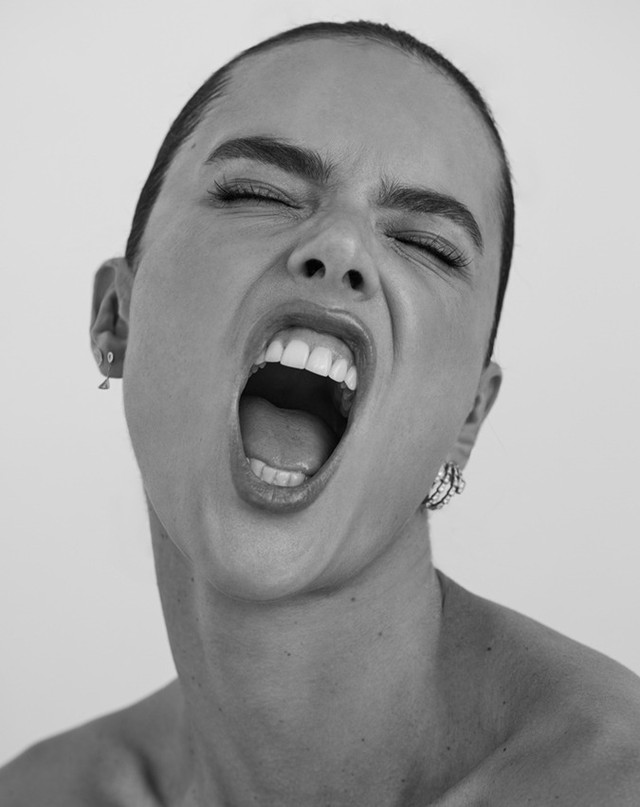 Black and white portrait of an adult woman with her mouth wide open and eyes squinted shut, posing in front of a plain white background.